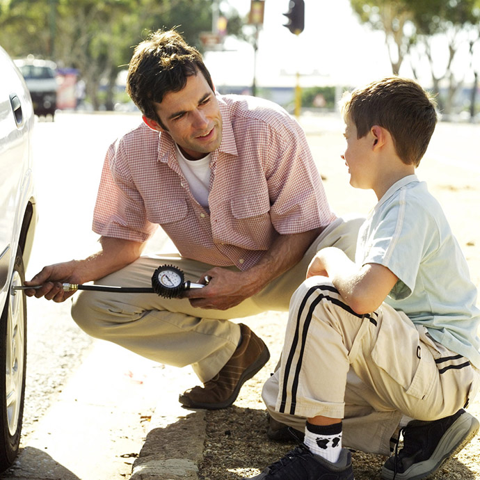 Young Man Checking the Air Pressure of Car Tire with His Son