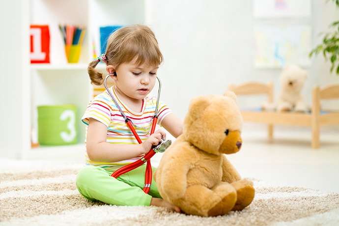 kid girl playing doctor with plush toy at home
